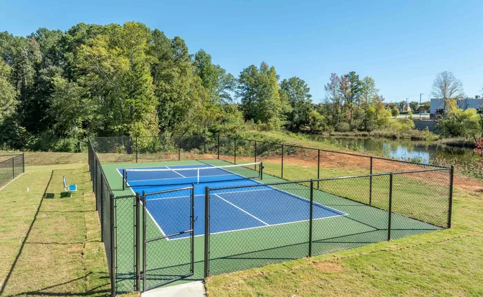 Beautiful outdoor tennis court surrounded by lush greenery and serene pond
