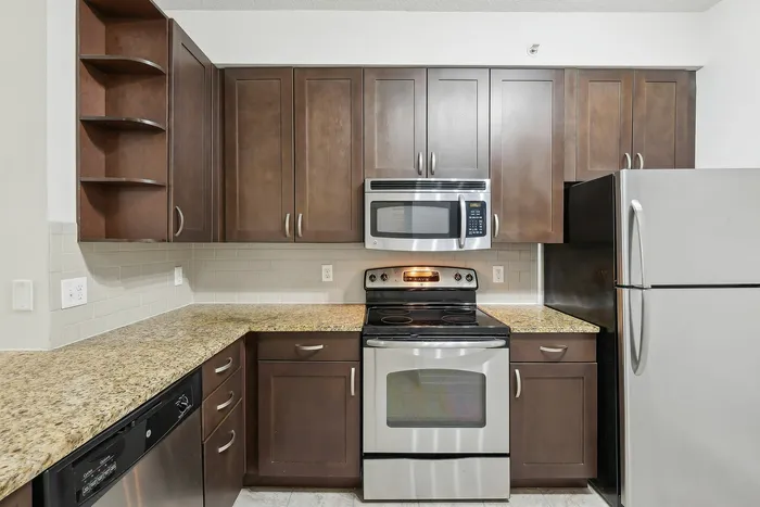 Delray Beach, FL, Apartments Near Tri-Rail Station - Congress Grove - Modern Kitchen With Dark Wood Cabinets, Granite Countertops, Subway Tile Backsplash, And Stainless Steel Appliances.