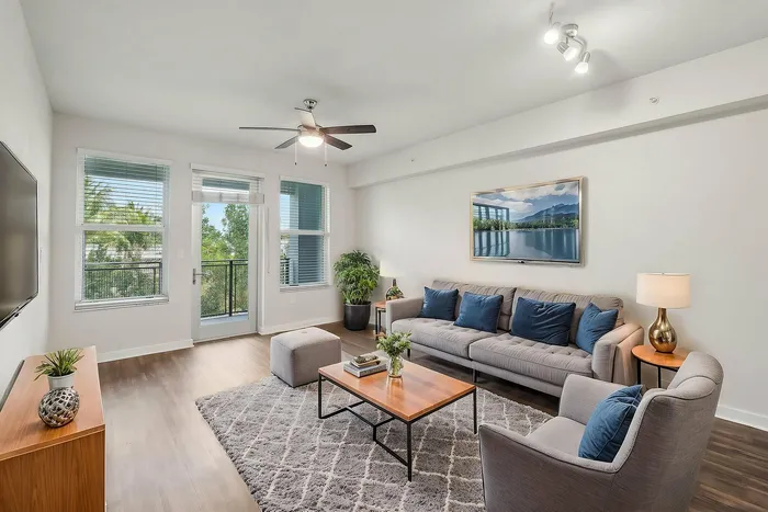 Delray Beach, FL, Apartments Near Florida Atlantic University (FAU) - Congress Grove - Living Room With Hardwood-Style Plank Floor, Gray Sofa, Coffee Table, Ceiling Fan, And Glass Door To Balcony.