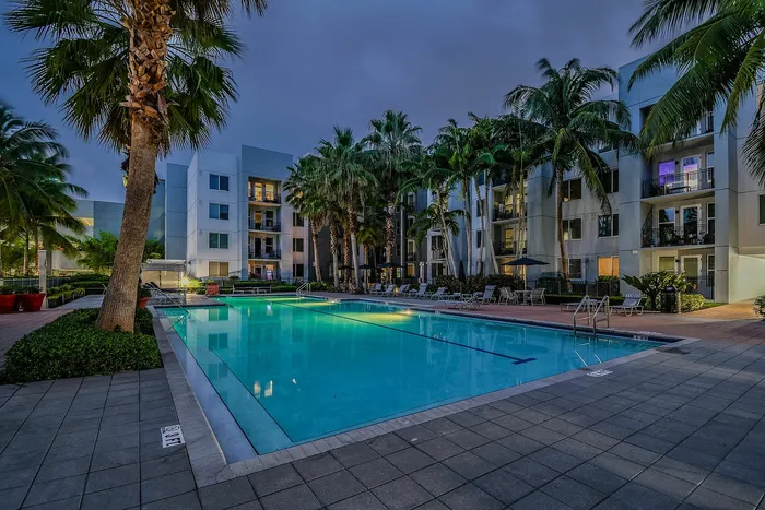Two-Bedroom Apartments in Delray Beach, FL - Congress Grove - Resort Style Pool At Dusk With Palm Trees, Poolside Lounge Chairs, And Modern Apartment Buildings Surrounding The Deck.