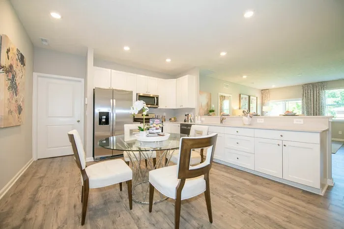 Avon, IN, Homes for Rent Near Indianapolis International Airport - Woods at Countryside Crossing - Gourmet Kitchen with Hardwood-Style Flooring, Energy Efficient Stainless Steel Appliances, White Cabinetry, Granite Countertops, and Dining Area with a Glass Table and Chairs.