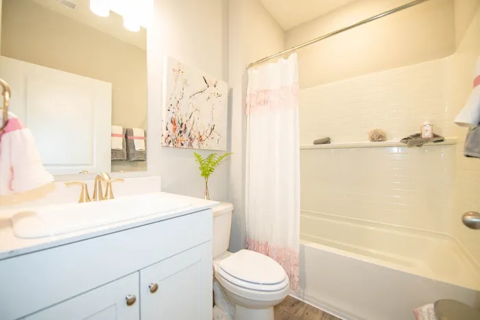 Avon, IN, Homes for Rent Near Sams Club - Woods at Countryside Crossing - Bathroom with Bath and Shower, Tile Backsplash, White Vanity, Large Mirror, and Hardwood-Style Flooring.