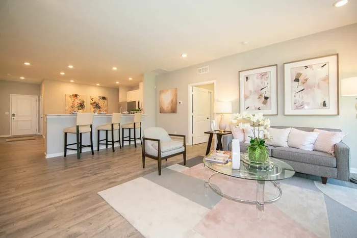 Furnished living room with windows, sliding glass door, rug, couch, and lamps with view of kitchen
