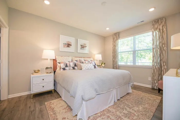 Three-Bedroom Homes for Rent in Avon, IN - Woods at Countryside Crossing - Bedroom with Hardwood-Style Flooring, Area Rug, Bed, Nightstands with Lamps, Corner Chair, Dresser, and Large Window with Blinds.