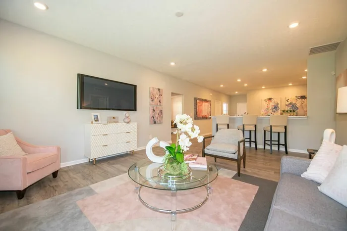 3-Bedroom Homes for Rent in Avon, IN - Woods at Countryside Crossing - Living Room with Hardwood-Style Flooring, Area Rug, Sofa, Armchairs, Glass-Top Coffee Table, Storage Cabinet, Wall-Mounted TV, and View of Breakfast Bar.