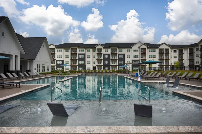 Athens, AL Apartments Near Huntsville - Gateway Village - Outdoor POol Area with a Large Blue Pool, Submerged Seating, Poolside Lounge Chairs, Umbrellas, and Turf