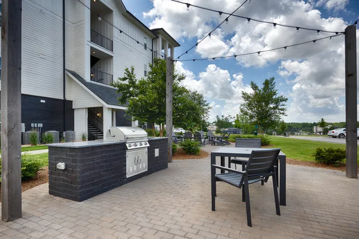 Athens, AL, Luxury Apartments - Gateway Village - Outdoor Grilling Area with Gas Grills, Decorative Lights, and a Table and Chairs with Access to the Fire Pits
