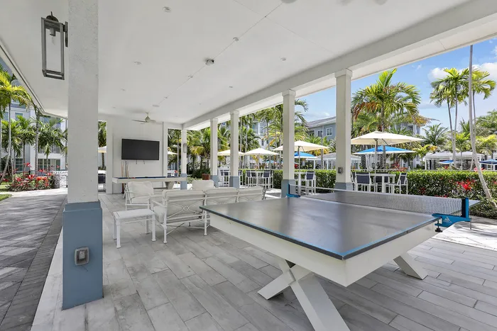 1-Bedroom Apartments in Lantana, FL - Ivory Lantana - Open-Air Pavilion with Ping-pong Table, Mounted TV, Ceiling Fans, and Umbrella Tables with Chairs Along the Side.