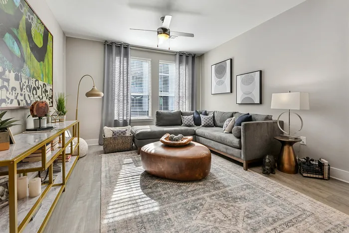 Pet-Friendly Luxury Apartments in Sandy Springs, GA - The Morgan Sandy Springs - Living Room with Wood-Style Flooring, Sectional Couch, Coffee Table, Side Table, Lamps, Console Table, and Ceiling Fan.