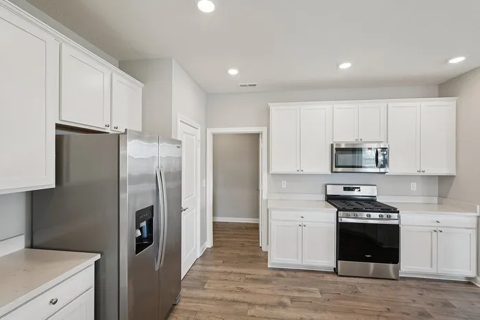 3-BR Homes in Whitestown, IN - Prairie Chase - Kitchen with Hardwood-Style Flooring, White Cabinetry, And Stainless Steel Appliances.