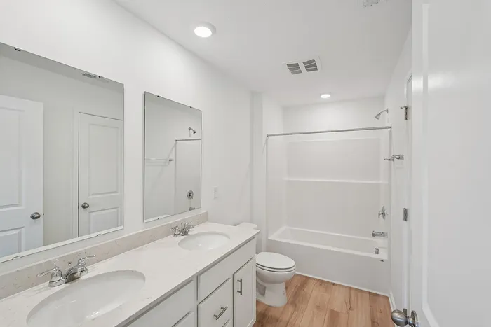 Three-BR Homes in Whitestown, IN - Prairie Chase - Bathroom With Hardwood-Style Flooring, Double Vanity, Two Mirrors, White Cabinetry, Light Fixtures, Bathtub And Shower Combo.