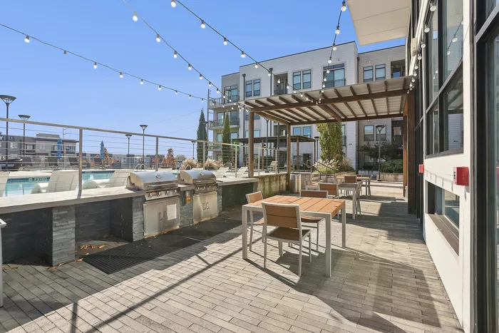 1-Bedroom Luxury Apartments in Sandy Springs, GA - The Morgan Sandy Springs - Grilling Station with Built-In Stainless Steel Grills, Countertops, Dining Tables and Chairs, Pergola, and String Lights.