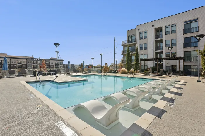Two-Bedroom Luxury Apartments in Sandy Springs, GA - The Morgan Sandy Springs - Swimming Pool with Spacious Sundeck, In-Water Loungers, Pergola, and View of the Apartments.