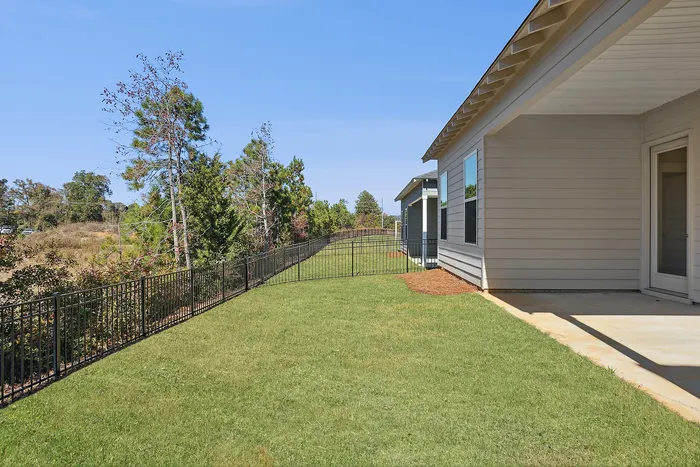 Opelika, AL, Townhomes near Auburn University - Champions Square - Private Fenced Backyard With Covered Patio, Green Lawn, And Tree-Lined Views Beside Modern Home Exterior.