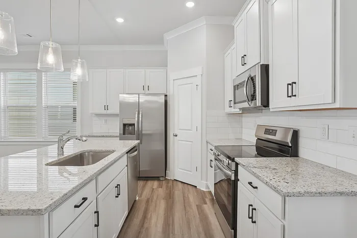Opelika, AL, Homes near Auburn University - Champions Square - Bright White Kitchen With Quartz Countertops, Stainless Steel Appliances, Subway Tile Backsplash, And Pendant Lights.
