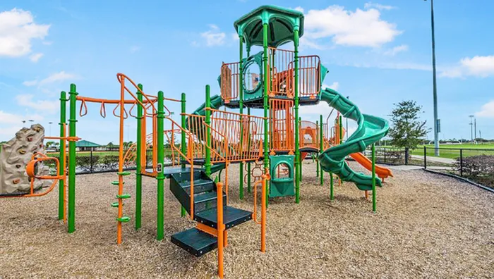 Four-Bedroom Homes in Poinciana, FL - The Preserve at Poinciana - Community Playground With Colorful Slides, Climbing Structure, and Mulch Surface Beside Open Park Space and Fenced Fields.