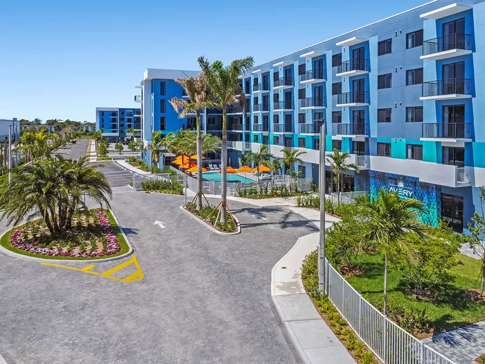 Modern apartment complex showcasing vibrant blue exteriors, lush palm trees, and a refreshing pool area under clear skies.