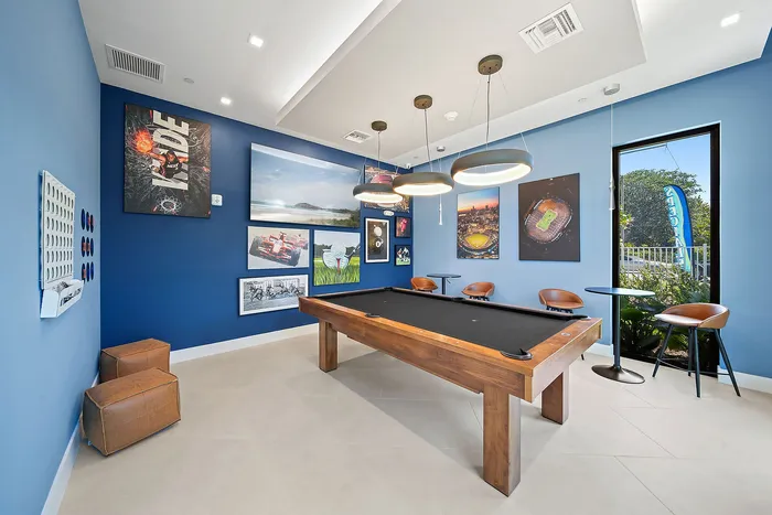 Chic entertainment room with a black pool table, stylish seating, and vibrant sports-themed wall art, illuminated by modern pendant lights.