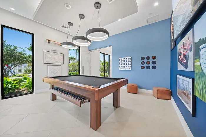 Modern recreational room with a sleek pool table, artistic wall decor, and large windows offering lush garden views.