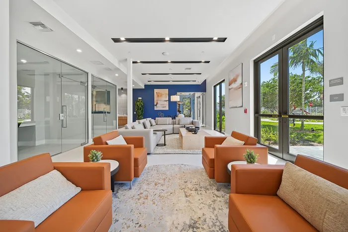 Luxurious apartment lounge with modern orange seating, sleek glass walls, and vibrant natural light creating a welcoming atmosphere.