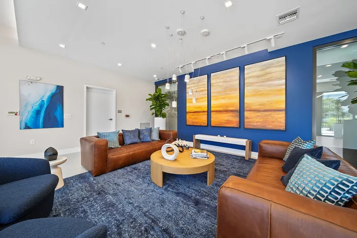 Modern clubroom with vibrant blue and orange artwork, luxurious leather sofas, and elegant lighting, perfect for stylish relaxation.