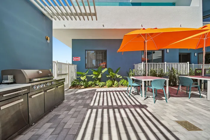 Chic outdoor patio with vibrant orange umbrellas, modern grill, and stylish seating, perfect for entertaining.