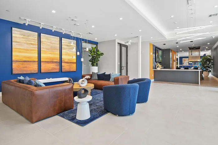 Modern apartment common area with chic leather seating, vibrant blue accents, and striking sunset wall art.