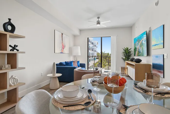 Modern living room with elegant dining setup, spacious seating area, and a large glass door leading to a balcony with scenic views.