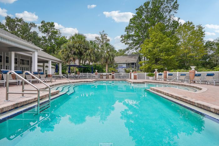 Inviting outdoor pool area with lush green surroundings, featuring palm trees, comfortable loungers, and a serene atmosphere.