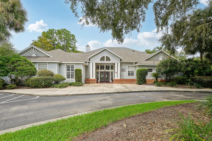 Charming single-story clubhouse with elegant arched windows, surrounded by lush greenery and a welcoming front pathway.