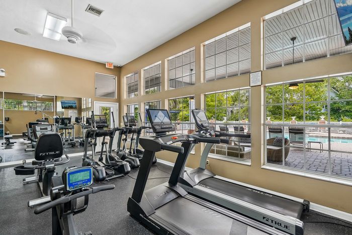 Bright and airy gym with modern cardio equipment and large windows overlooking a pool patio.