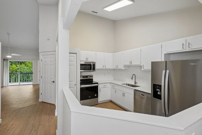 Bright modern kitchen with stainless steel appliances and spacious open-concept living room with lush greenery view.