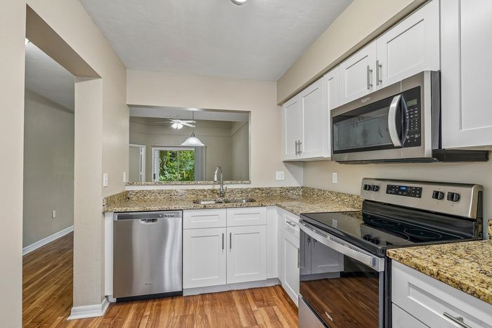 Modern kitchen with stainless steel appliances, granite countertops, and elegant white cabinetry, featuring a view into a bright dining area.