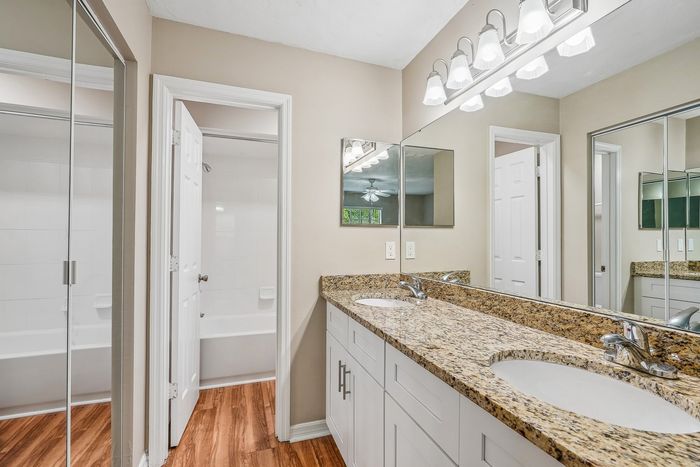 Elegant bathroom featuring a dual-sink granite countertop, chic lighting, and mirrored cabinets, with a pristine bathtub in the background.