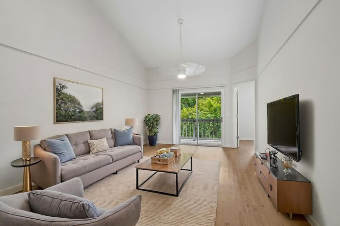 Elegant living room with modern decor, featuring a cozy sofa, plush armchair, and a large window offering lush green views.