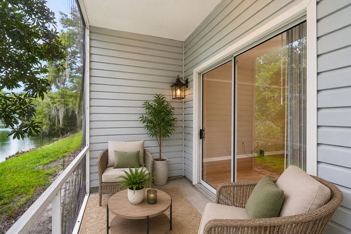 Inviting screened patio with cozy wicker chairs, lush greenery, and a serene lake view.