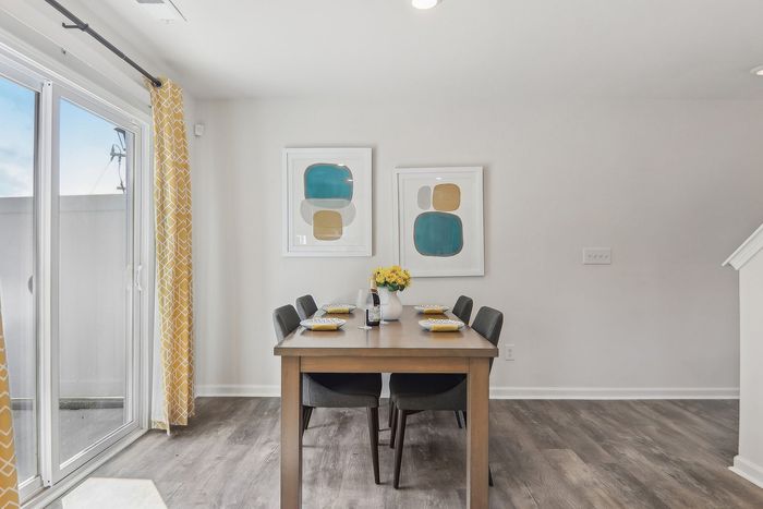 Chic dining area with elegant wooden table, modern chairs, and vibrant artwork. Large sliding doors with yellow patterned curtains offer bright natural light.