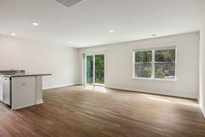 Bright and airy living space with elegant wood flooring, modern kitchen island, and large windows offering lush green views.
