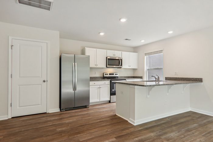 Modern kitchen with sleek stainless steel appliances, elegant white cabinetry, and an inviting breakfast bar against warm wooden floors.