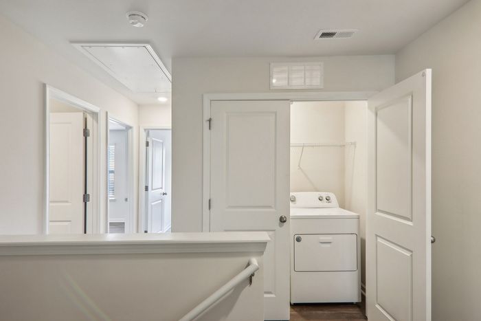 Bright hallway with three doors leading to separate rooms, showcasing a convenient in-unit laundry area with washer and dryer.