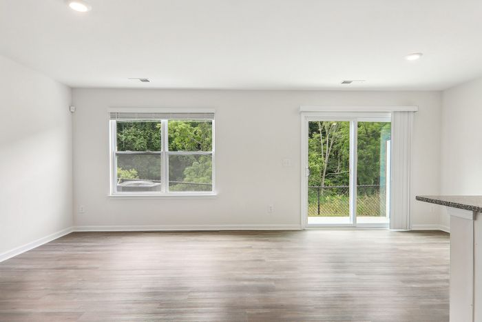 Bright and airy living space with large windows, sleek hardwood floors, and a charming view of lush greenery.