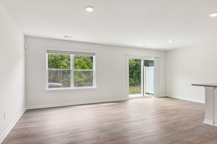 Bright and airy living space with large windows, modern laminate flooring, and access to a private patio.