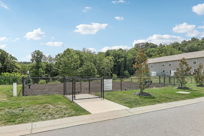 Charming fenced dog park surrounded by lush greenery and modern townhomes, perfect for outdoor enjoyment.