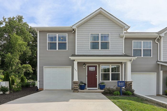 Elegant two-story gray townhouse with a welcoming red front door, attached garage, and vibrant green landscaping, perfect for modern family living.