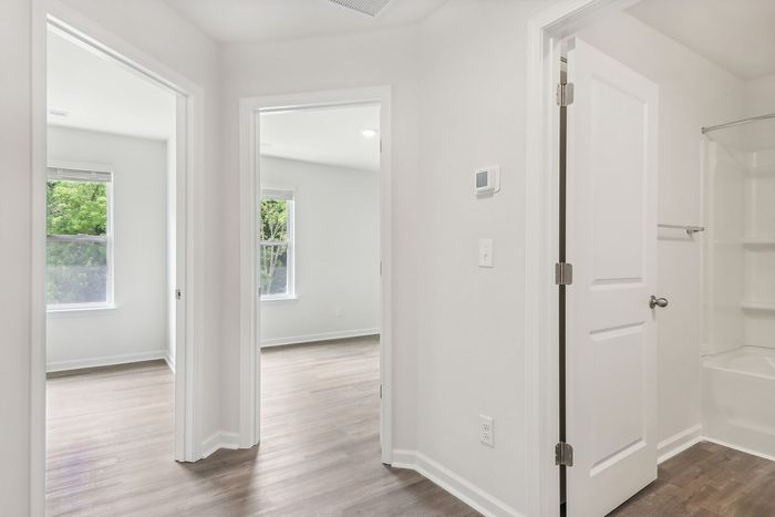 Bright and airy hallway leading to modern bedrooms with large windows and sleek hardwood floors.