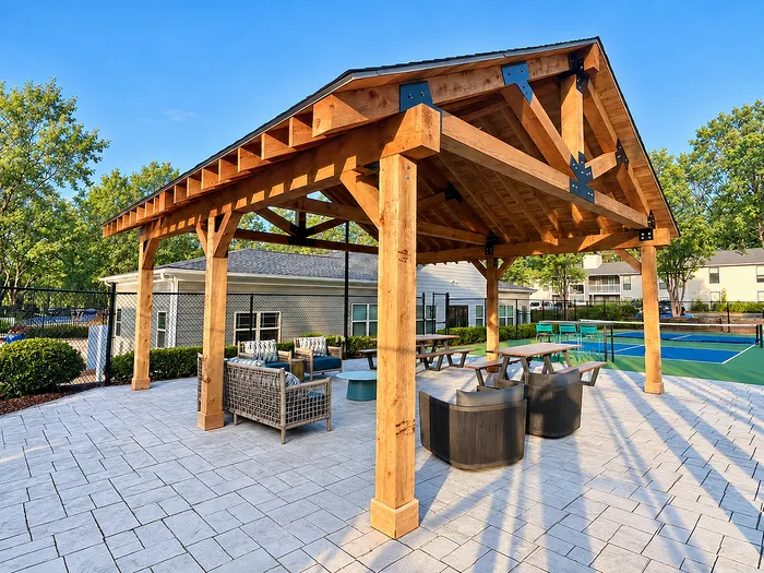 Inviting outdoor patio with wooden pergola, modern seating, and view of tennis courts in a lush residential area.