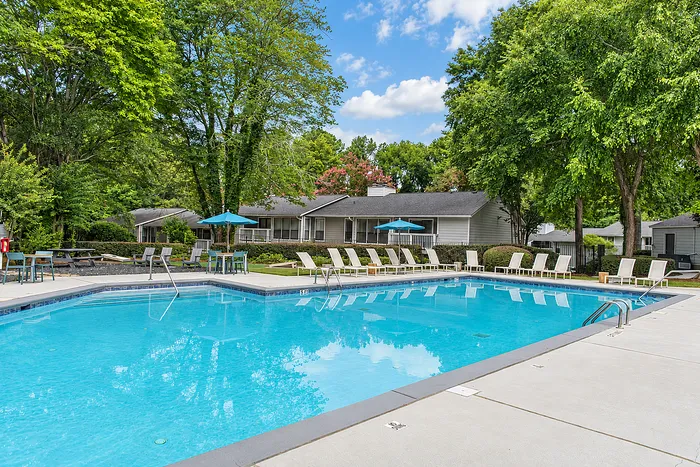 Inviting residential community with a sparkling blue pool, surrounded by lush greenery and relaxing lounge chairs.