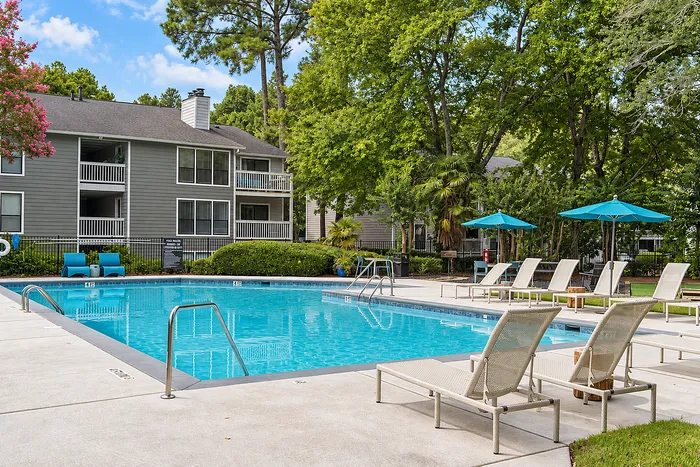 Elegant apartment complex with inviting outdoor pool, surrounded by lush greenery and comfortable lounge chairs for relaxation.