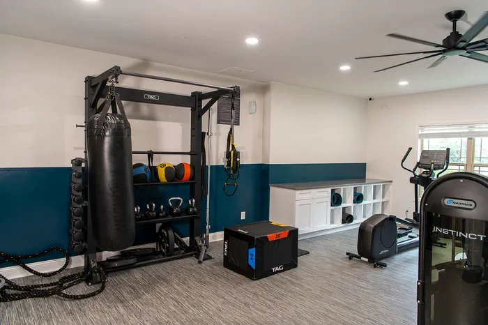 Modern home gym setup with diverse equipment, including kettlebells, medicine balls, and a power rack in a spacious, light-filled room.