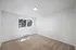 Spacious bedroom with large window and soft carpet flooring, illuminated by natural sunlight.